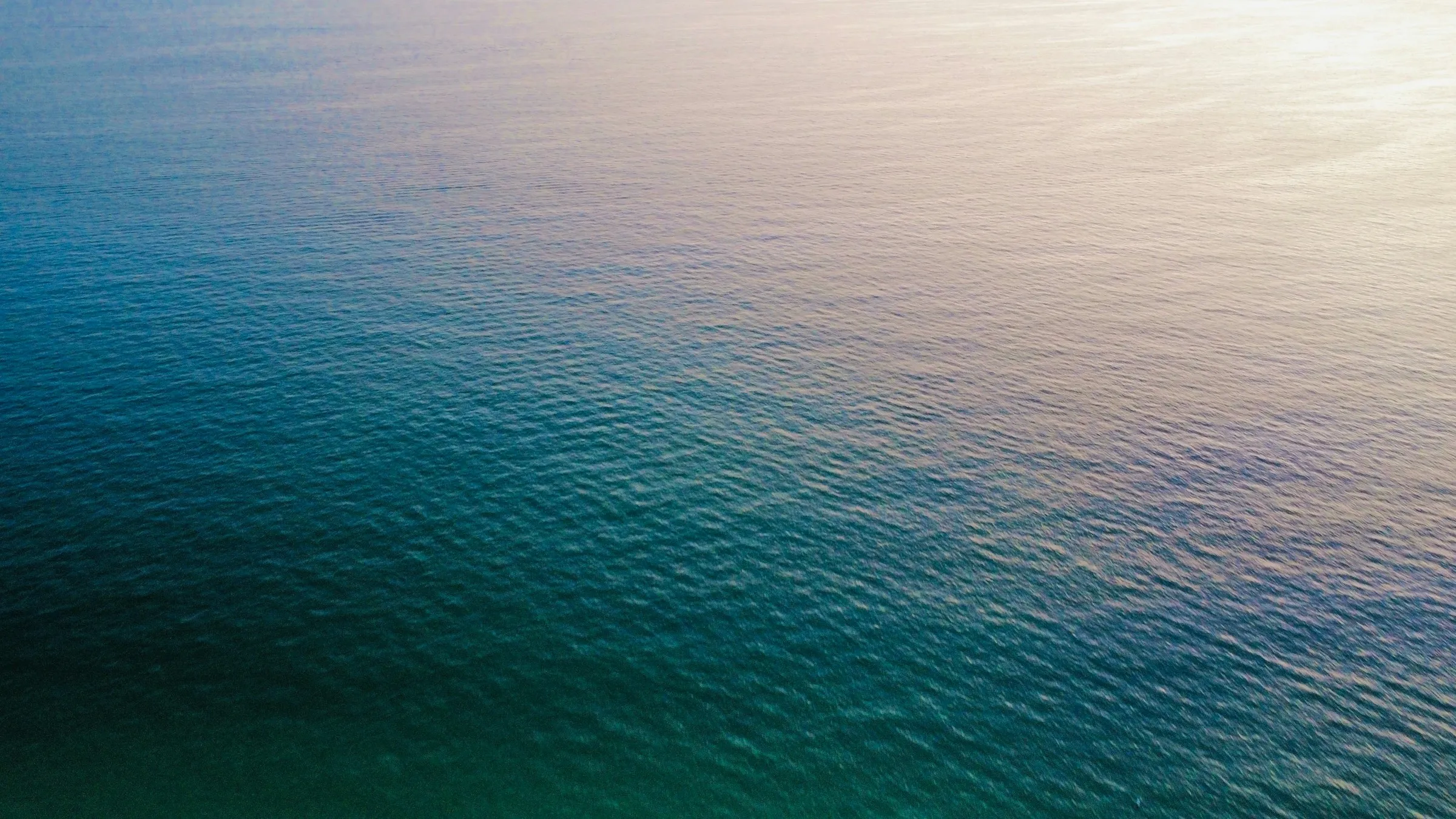 Open water seen from above, its colour shifting from deep green through blue to the glare of reflected sky